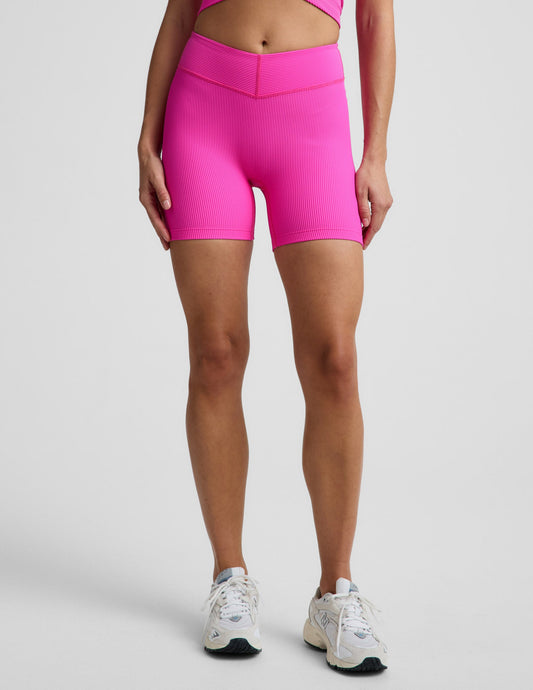 Woman wearing Pink Impulse Ribbed V-Waist 5" Biker Short paired with a matching pink crop top and cream sneakers.