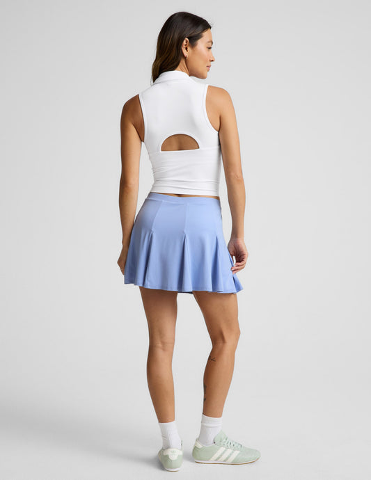 Woman wearing Blue Flounce This Way Skirt™ paired with a white cutout top and green sneakers, rear view.