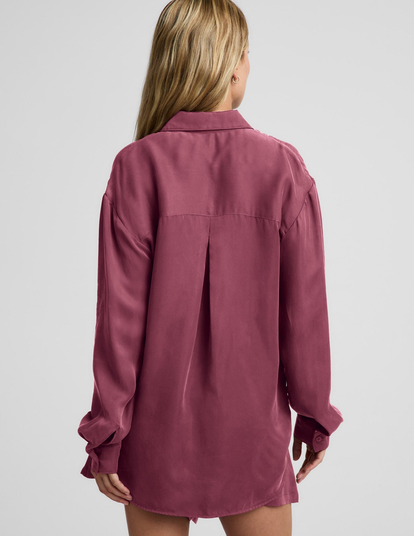 Woman wearing a purple button down shirt and shorts against a plain background.
