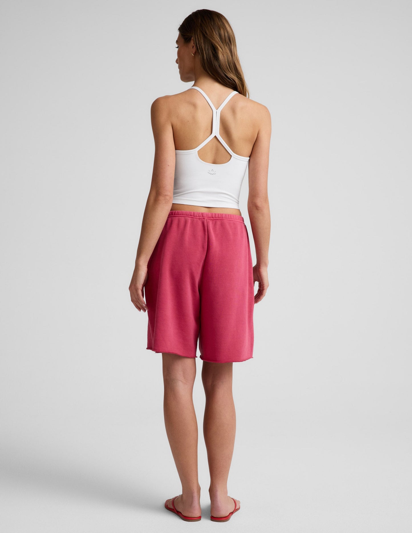 Woman wearing Pink Fade Out™ Low-Rise Bermuda Short, rear view, paired with a white racerback crop top.