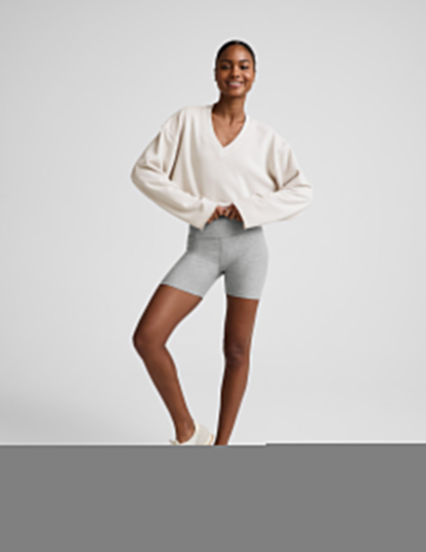 Woman wearing a white v-neck cropped sweatshirt and gray biker shorts against a plain background.