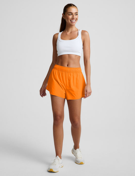 Woman wearing Orange Solemate™ 2.5" Short with a white sports bra, featuring a gathered elastic waistband and dolphin hem.
