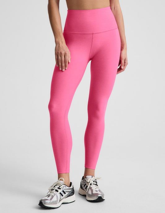 Woman wearing a pink bra and 7/8 length high waisted leggings against a plain background.