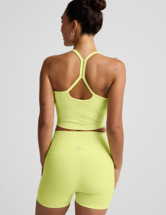 Woman wearing a bright yellow cropped racerback tank and biker shorts against a light gray background.