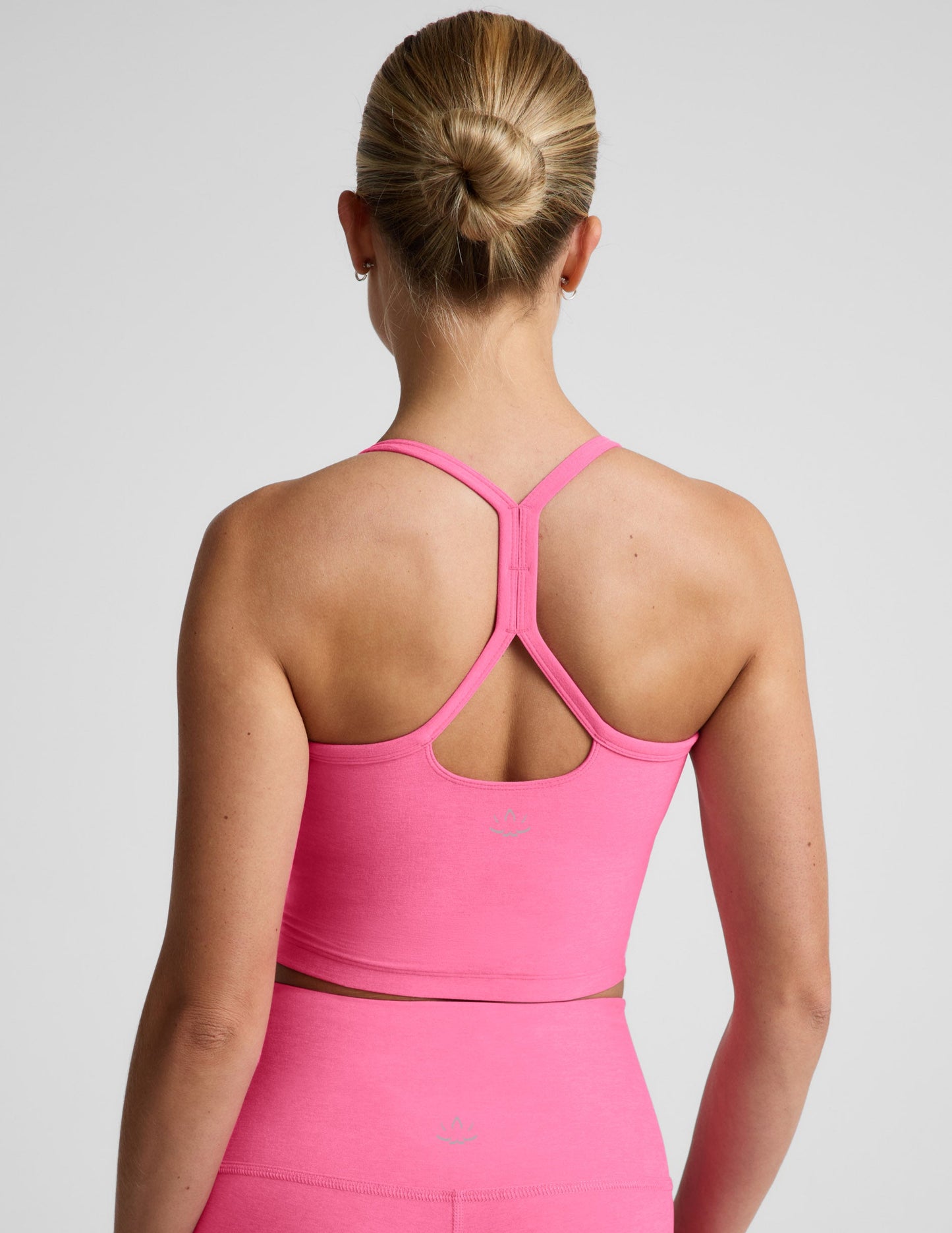 Woman wearing a pink cropped racerback tank top and leggings against a plain background.