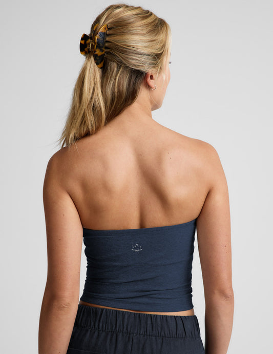 Woman wearing a navy strapless tank and navy linen pants against a plain background.