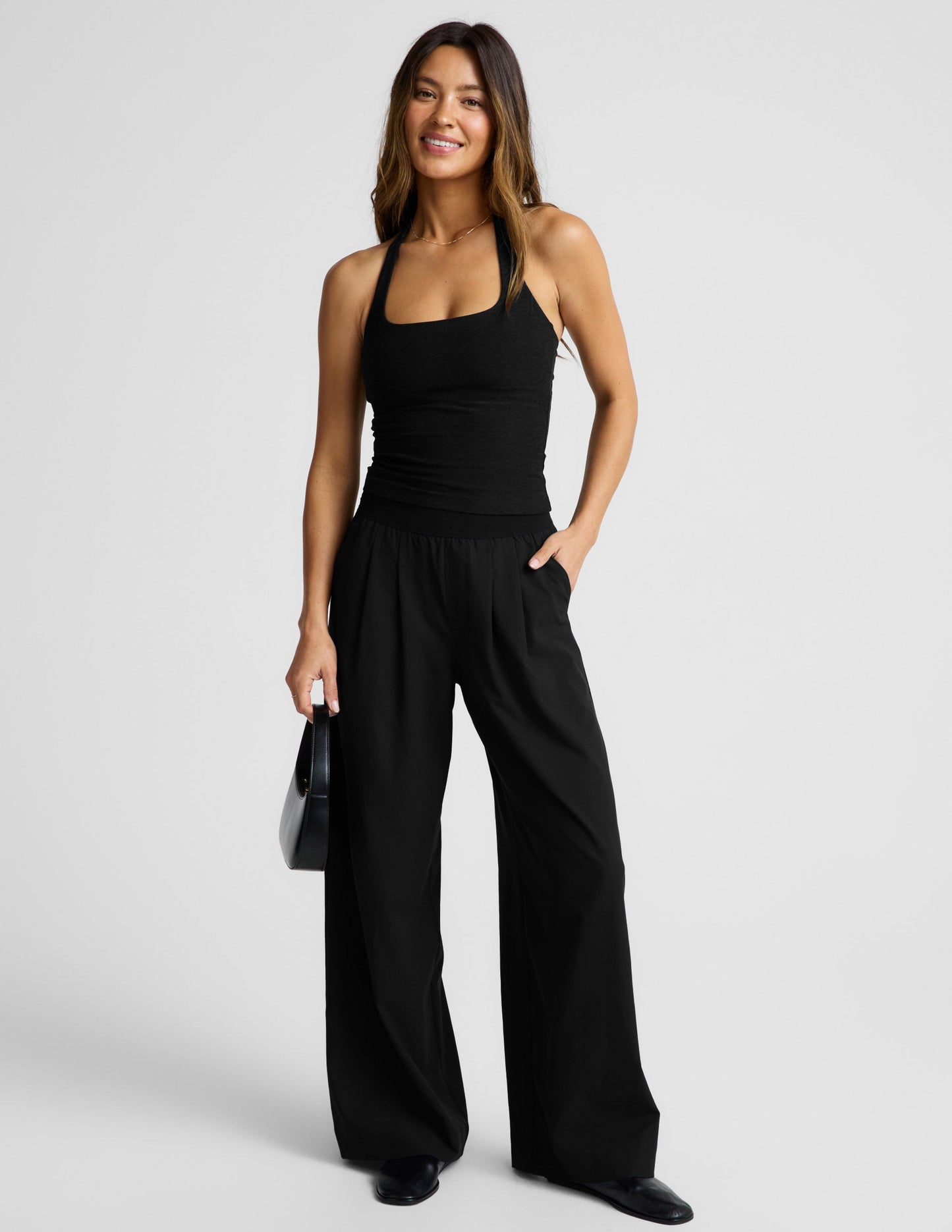 Woman wearing a black halter tank and black pants against a plain background.