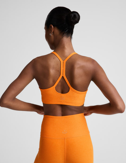 Woman wearing an orange sports bra and biker shorts against a plain background.
