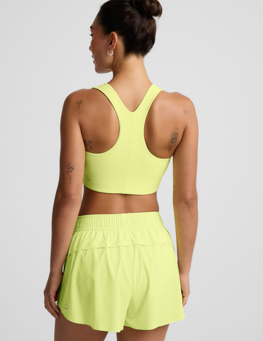 Woman wearing a bright yellow sports bra and shorts against a light gray background.
