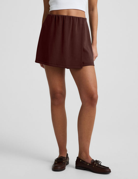 Woman wearing Brown Luxe Sandwash Skort™ paired with a white tank top and brown loafers.