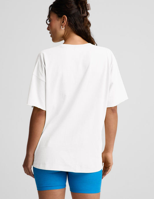 Woman wearing a white v-neck oversized t-shirt and blue biker shorts against a plain background.