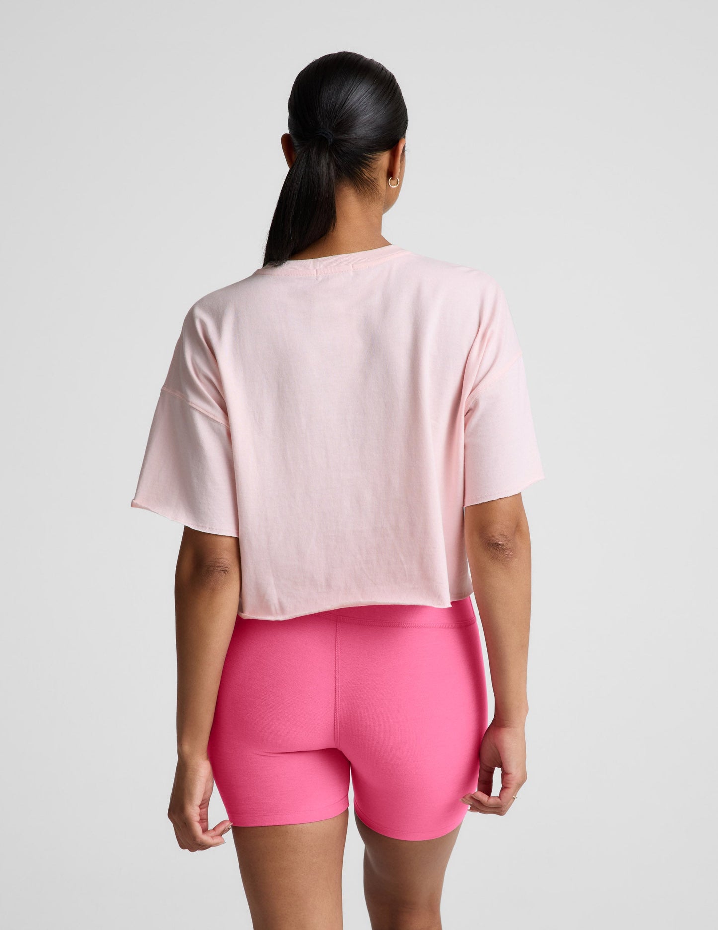 Woman wearing a light pink cropped t-shirt and pink biker shorts against a plain background.