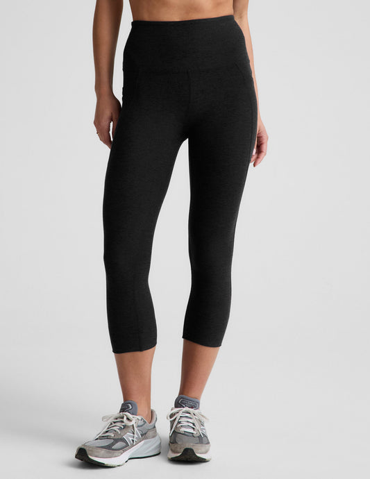 Woman wearing Black Spacedye™ Out Of Pocket High Waisted 20.5" Capri Legging with side pockets and grey sneakers.
