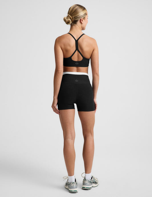 Woman wearing Black Spacedye™ Layered 3" Short, rear view, paired with a black sports bra and white sneakers.