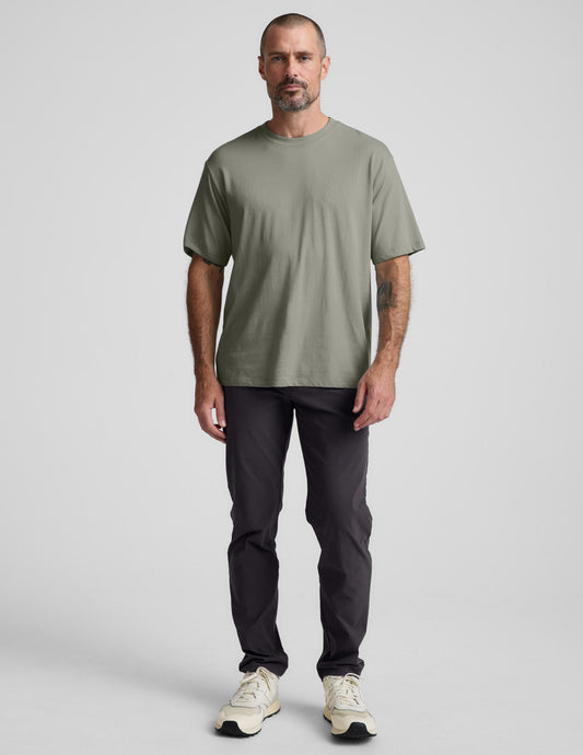 Man wearing a green cotton t-shirt and black pants against a plain background.