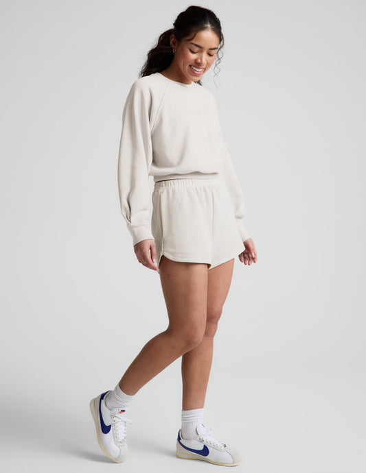 Woman wearing a white crew-neck and shorts against a plain background.
