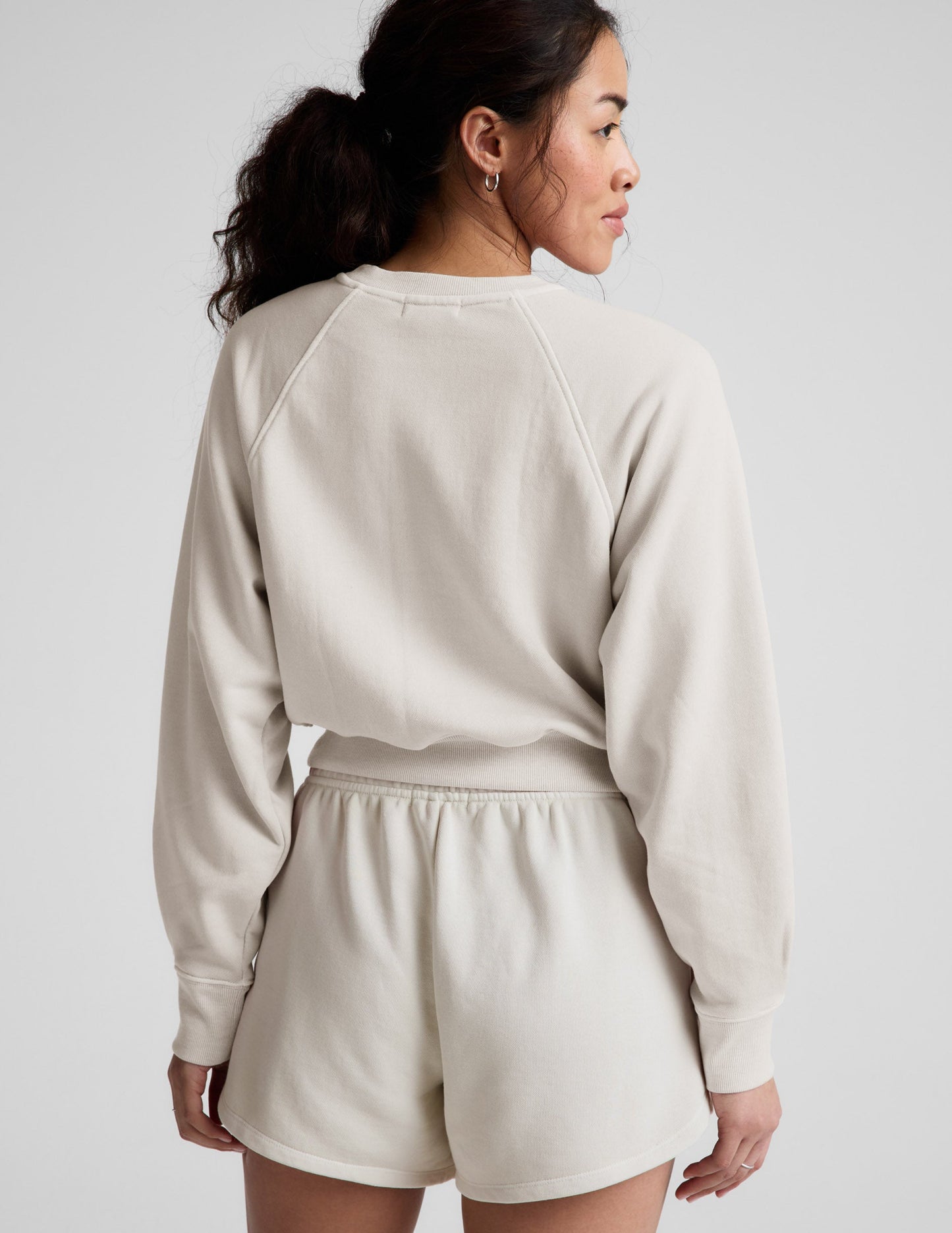 Woman wearing a white crew-neck and shorts against a plain background.