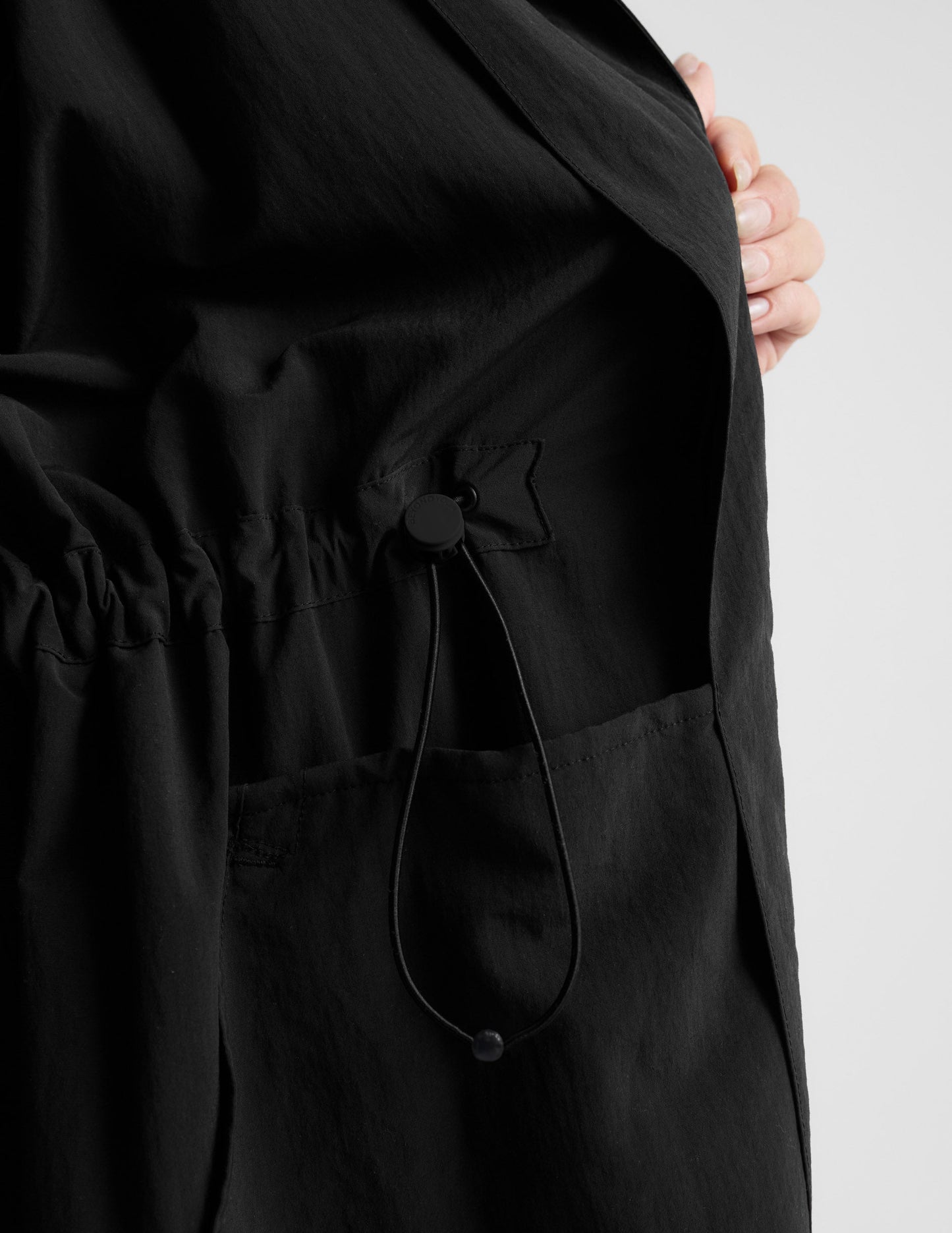 Woman wearing a black trench coat over a gray sports bra and leggings on a plain background.