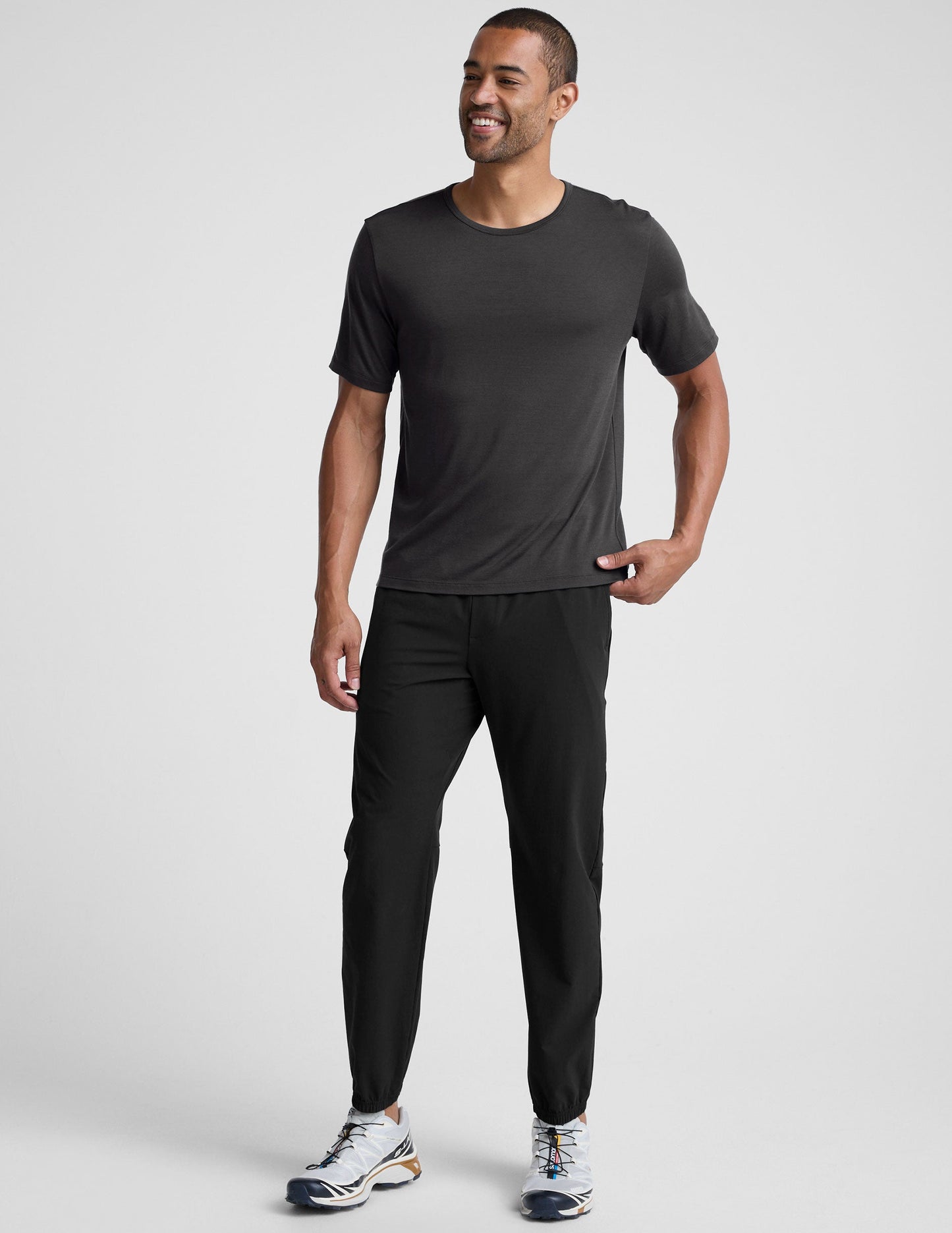 man wearing a black t-shirt and pants on a plain background.