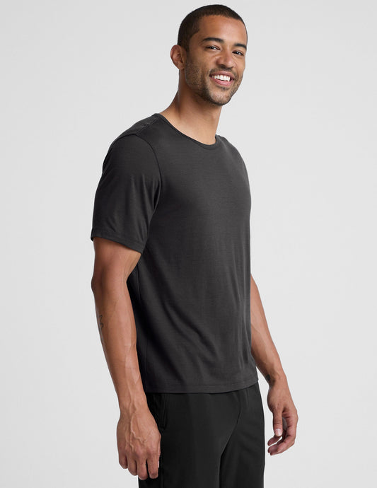 man wearing a black t-shirt and pants on a plain background.