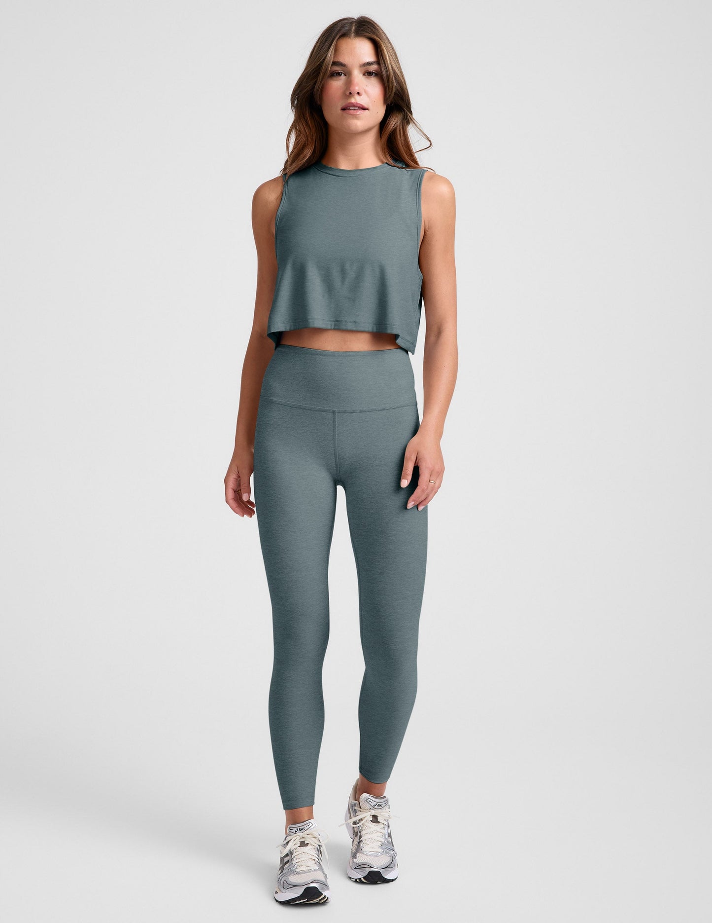 Woman wearing a gray sleeveless top and leggings on a light gray background.