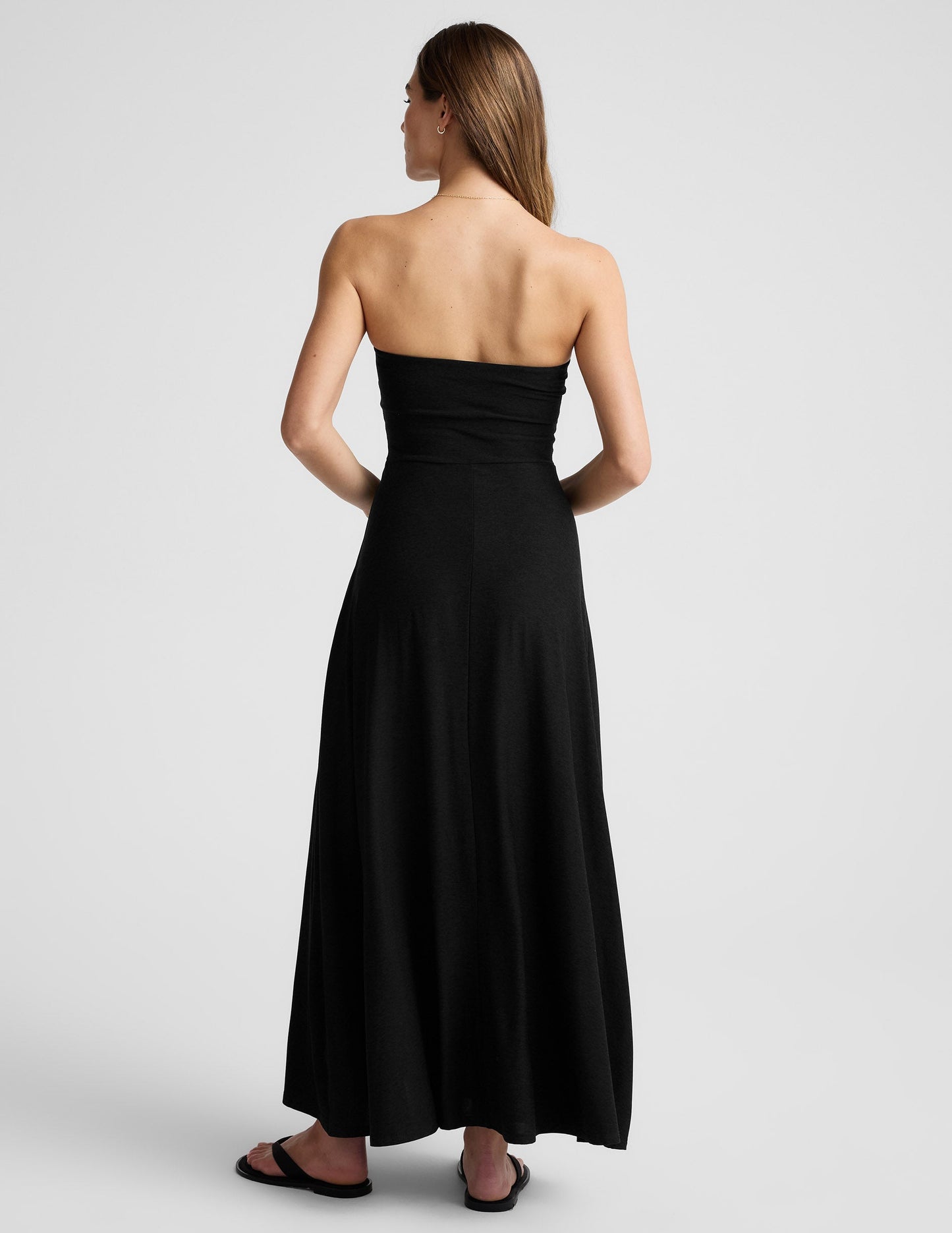 Woman wearing a black strapless maxi dress against a light gray background.