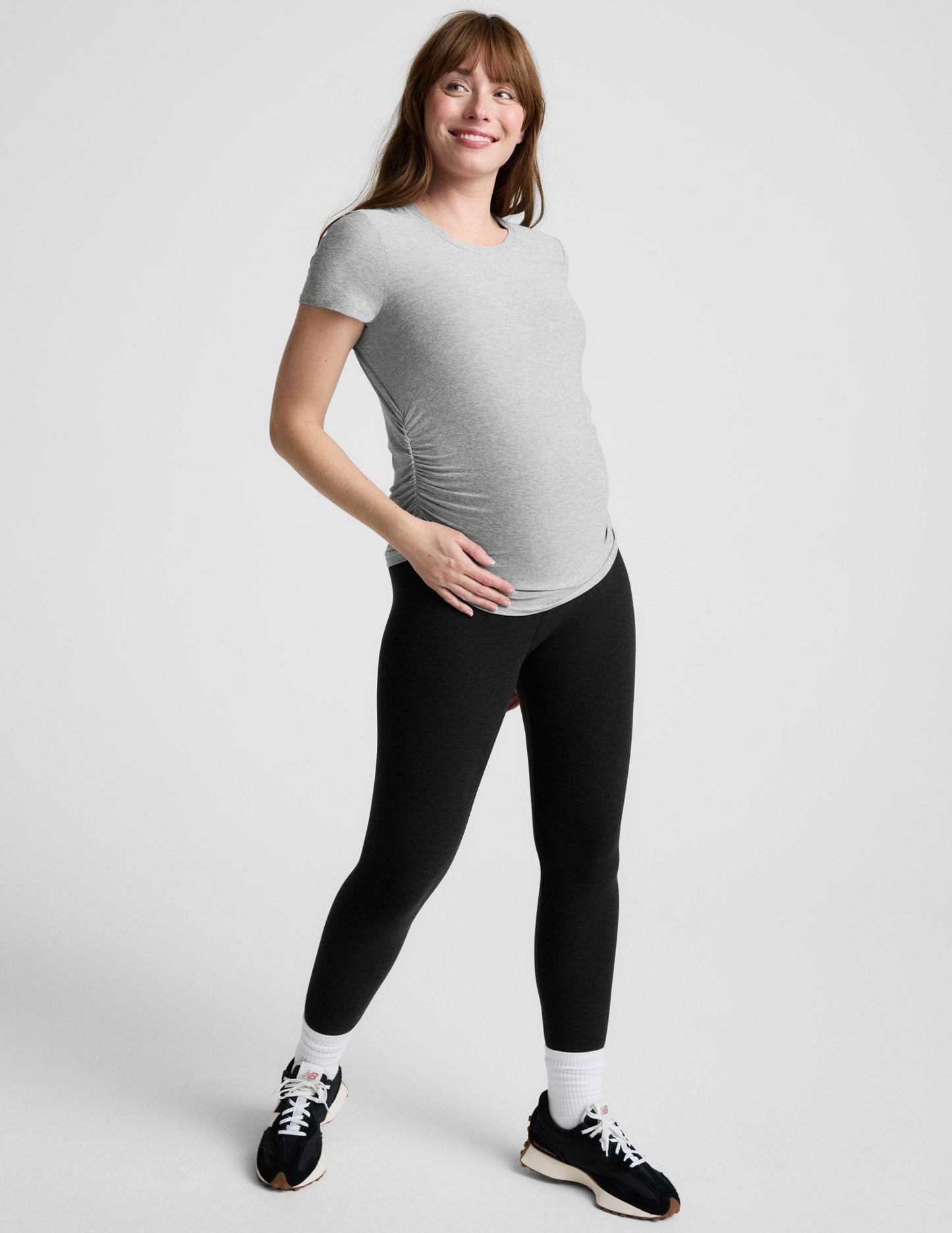 Woman wearing a gray maternity t-shirt and black leggings against a plain background.