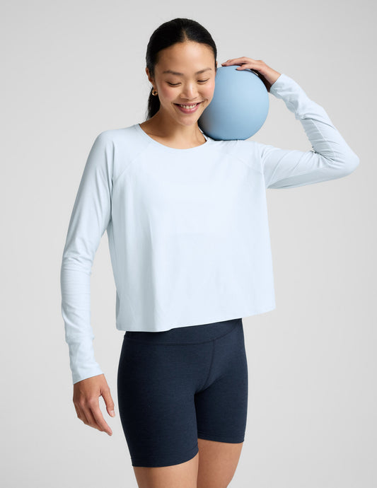 Woman wearing a light blue long sleeve and navy blue biker shorts against a plain background.