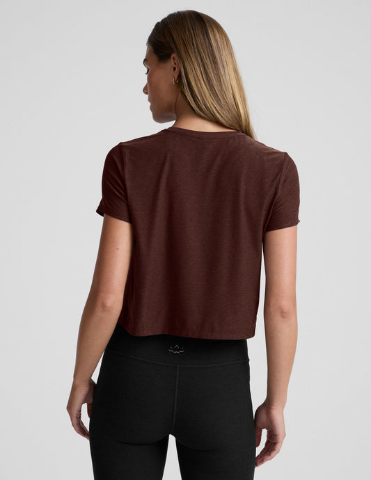 Woman wearing a brown cropped t-shirt and black bootcut pants against a plain background.