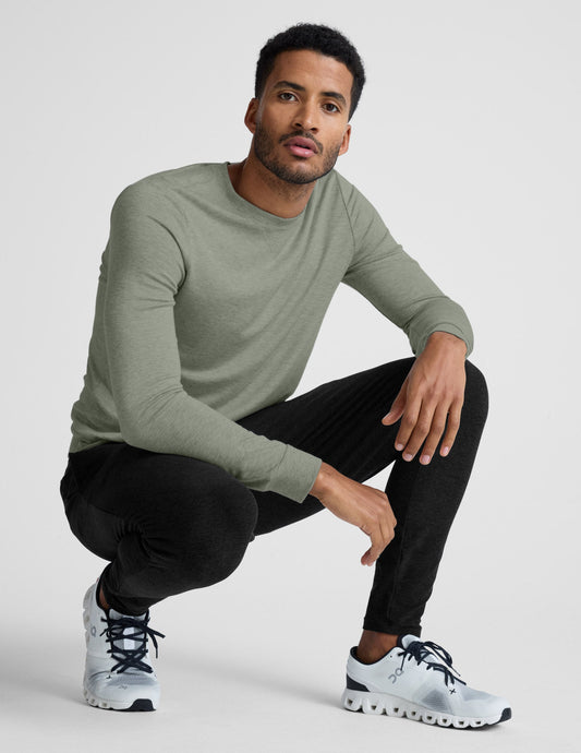 Man wearing a green long-sleeve shirt and black pants, sitting on a white background.