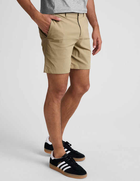 Side view of Essential Men's Chino 7" Short in beige with belt loops and pockets, hitting mid-thigh on a model.