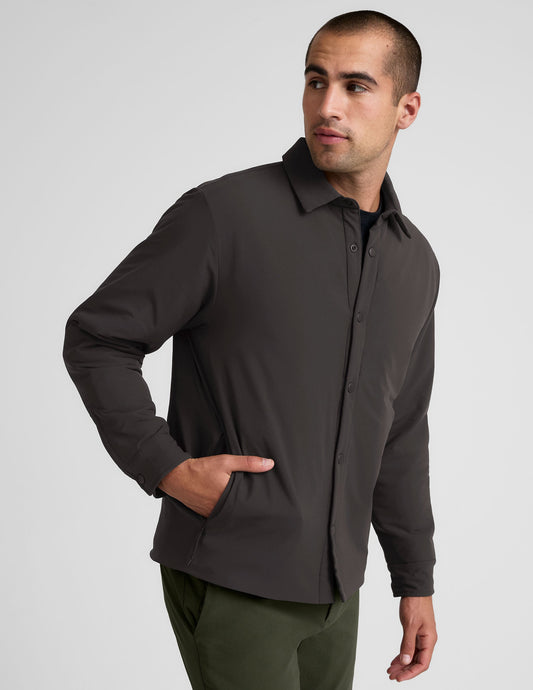 Man wearing a dark brown jacket over a black shirt with green pants on a light gray background.