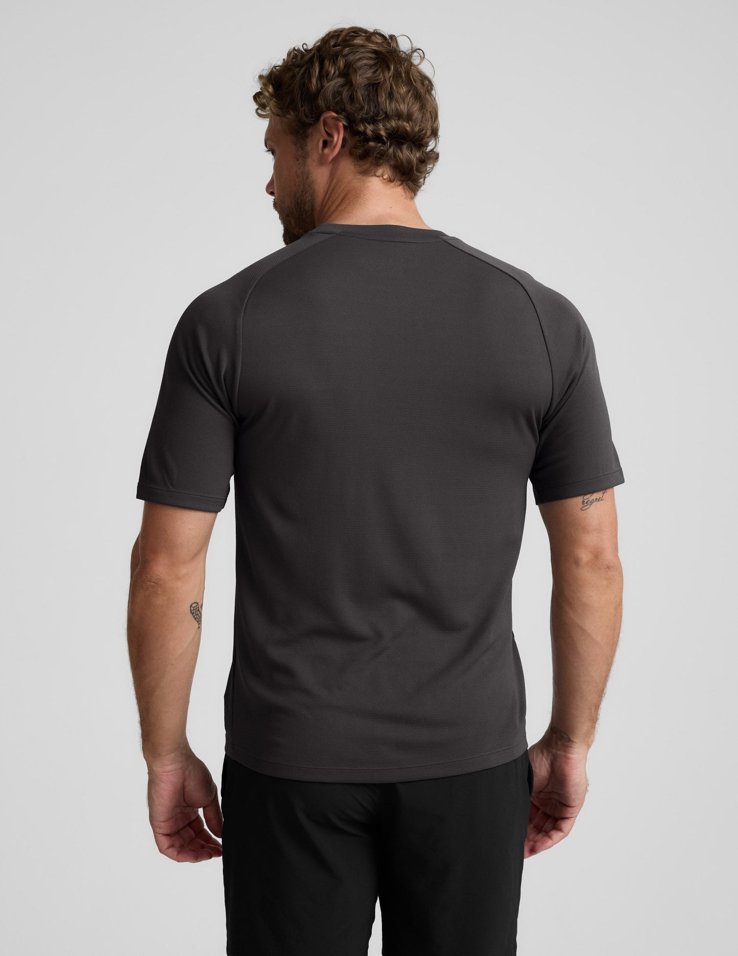Man wearing a black athletic short sleeve top and black shorts against a plain background.