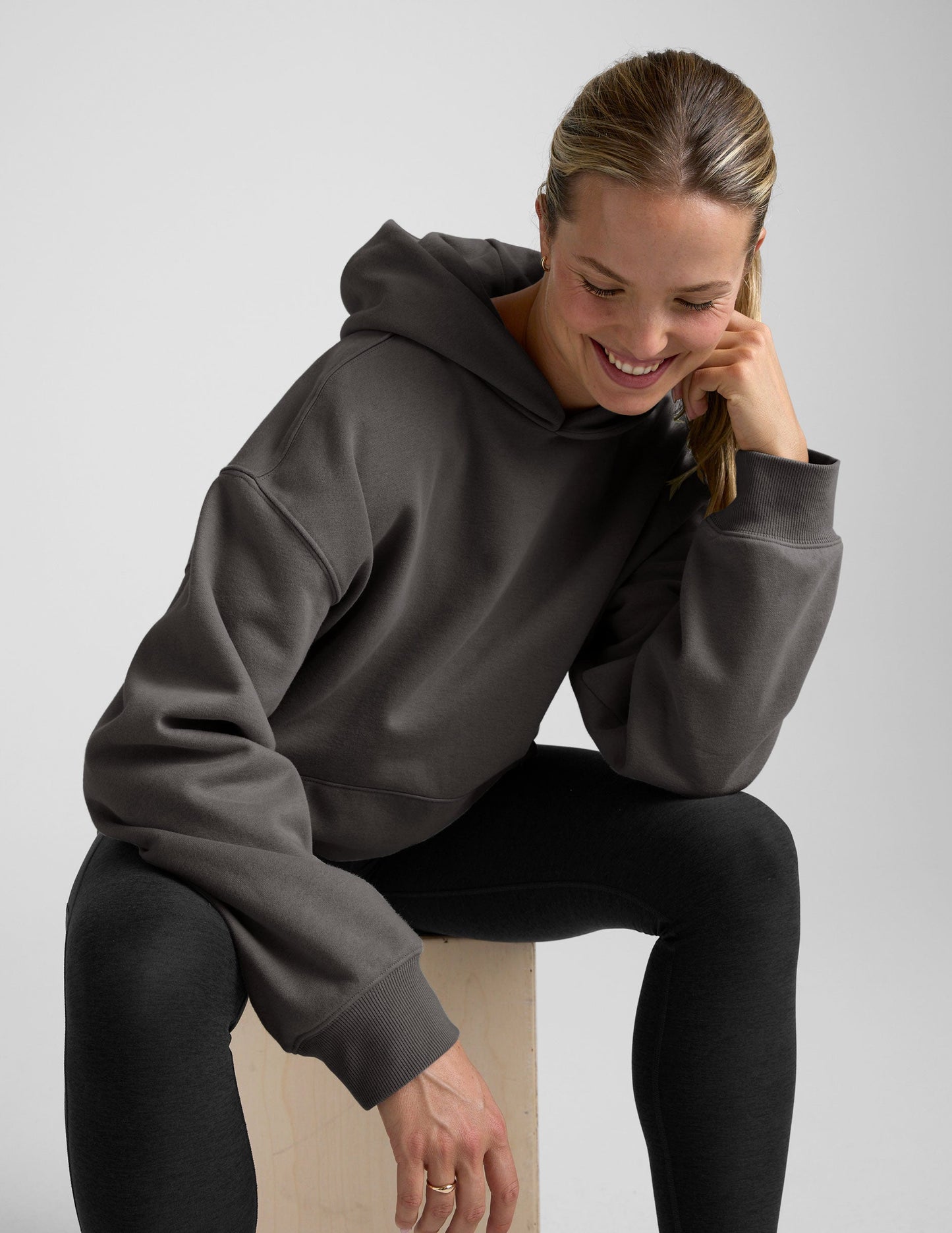 woman wearing a black hoodie with black leggings on a plain background.
