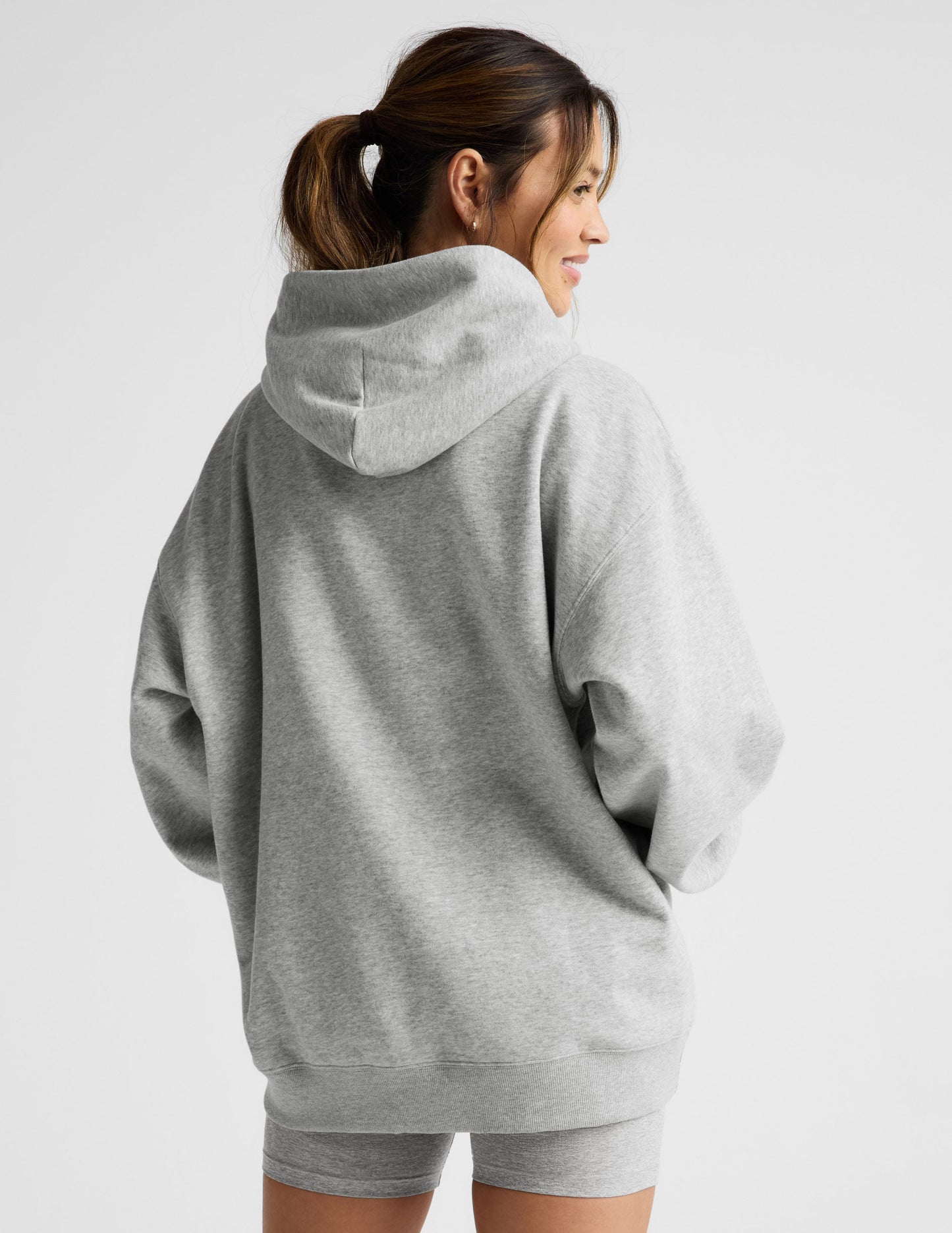 Woman wearing a gray hoodie and shorts set on a light gray background.
