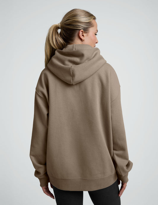 woman wearing a beige hoodie and black leggings on a plain background.