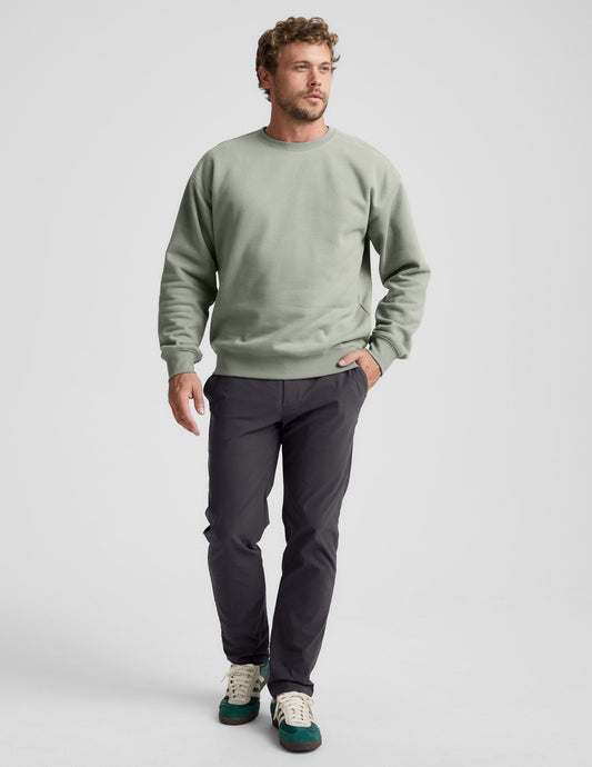 Man wearing a green crewneck sweatshirt and dark pants on a light gray background.