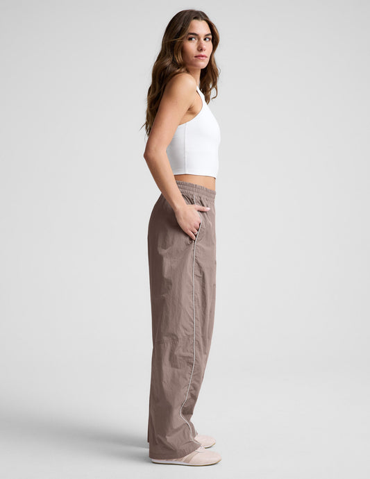 Side profile of the brown Limitless Mid-Rise Barrel Leg Pant with white piping, elastic waistband, and a relaxed fit.