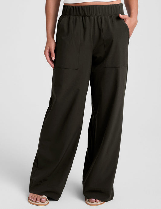 A woman wears dark green Easy Wide Leg Pants featuring an elastic waistband, side pockets, and a relaxed, flowy silhouette.