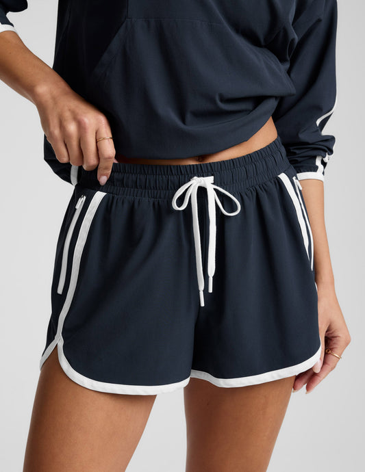 Woman wearing a blue quarter zip jacket and blue shorts with white trim against a plain background.