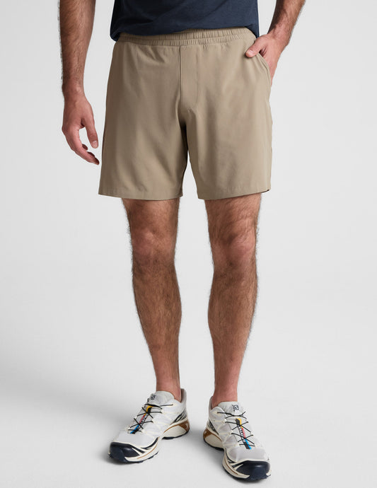 Front view of a man wearing beige Pivotal 2.0 Men's Lined Short 7" with an elastic waist and side pockets.