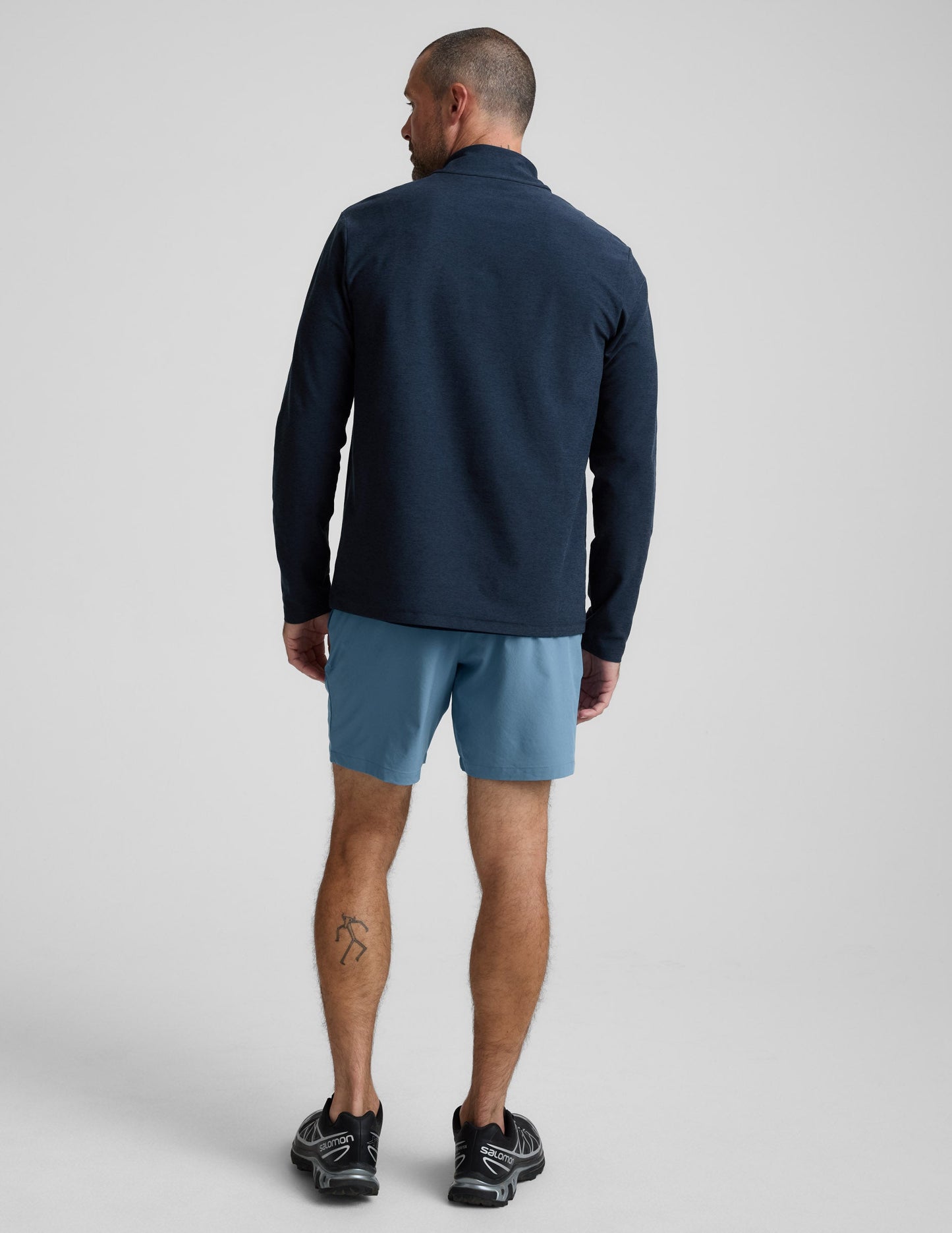 Rear view of man wearing Navy Pivotal™ 2.0 Men's Short 7" paired with a navy long-sleeve shirt and black sneakers.