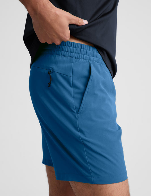 Side profile of man wearing Blue Pivotal 2.0 Men's Short 7"™ with a black shirt, showing the side pocket and zip detail.