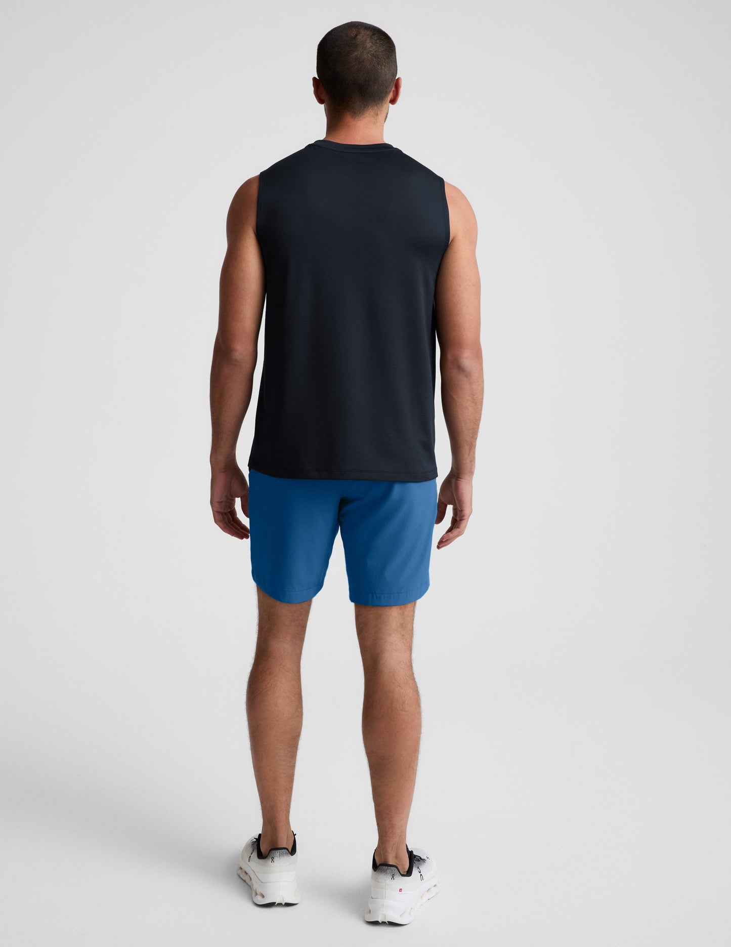 Man wearing Blue Pivotal 2.0 Men's Short 7™ from a rear view, paired with a black sleeveless top and white sneakers.
