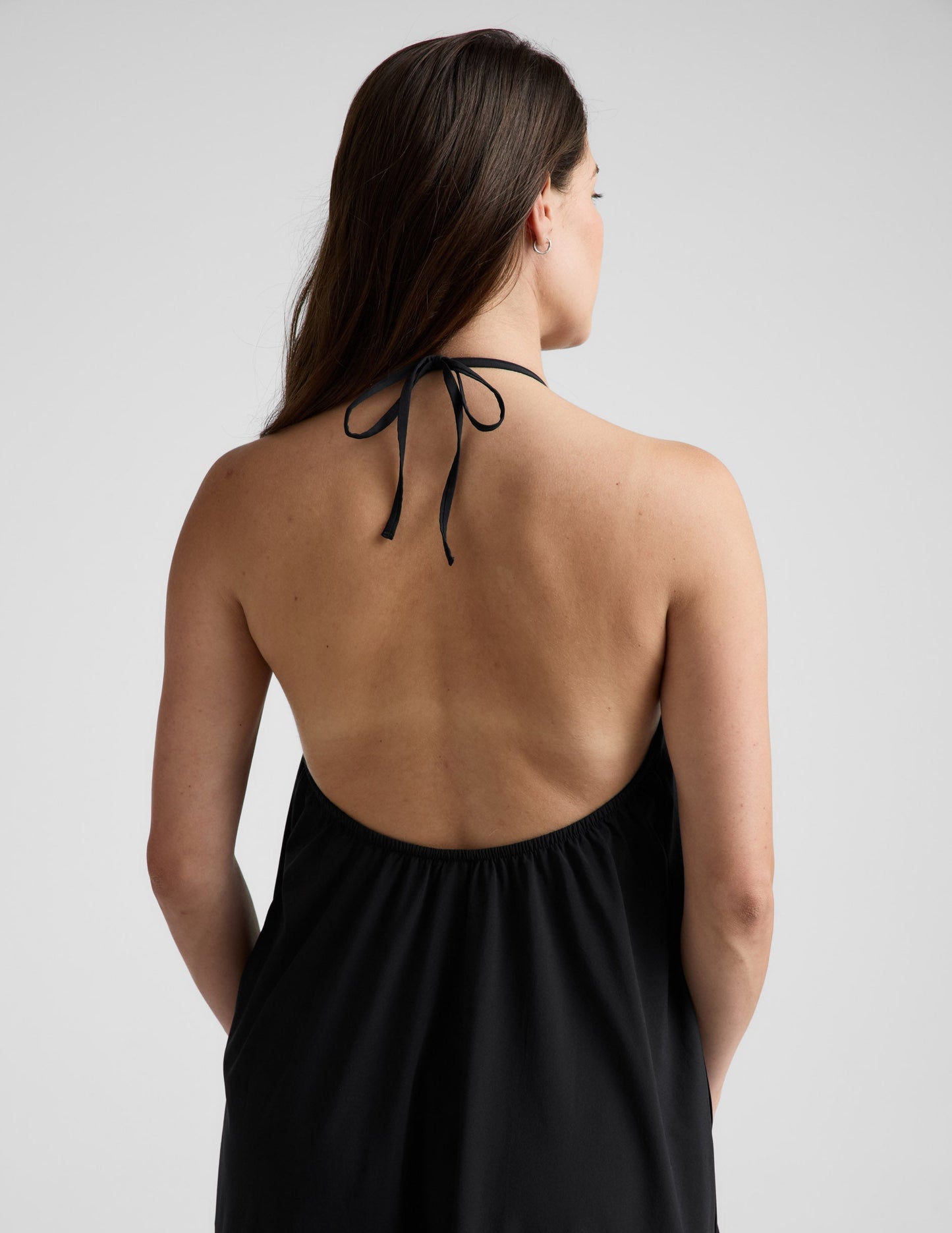 Woman wearing a black halter neck dress on a light gray background.