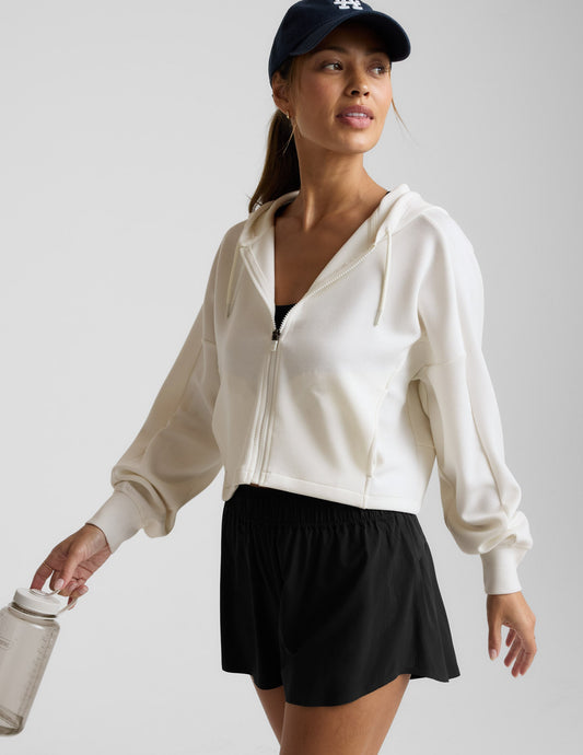 Woman wearing a white zip-up hoodie and black shorts against a plain background.