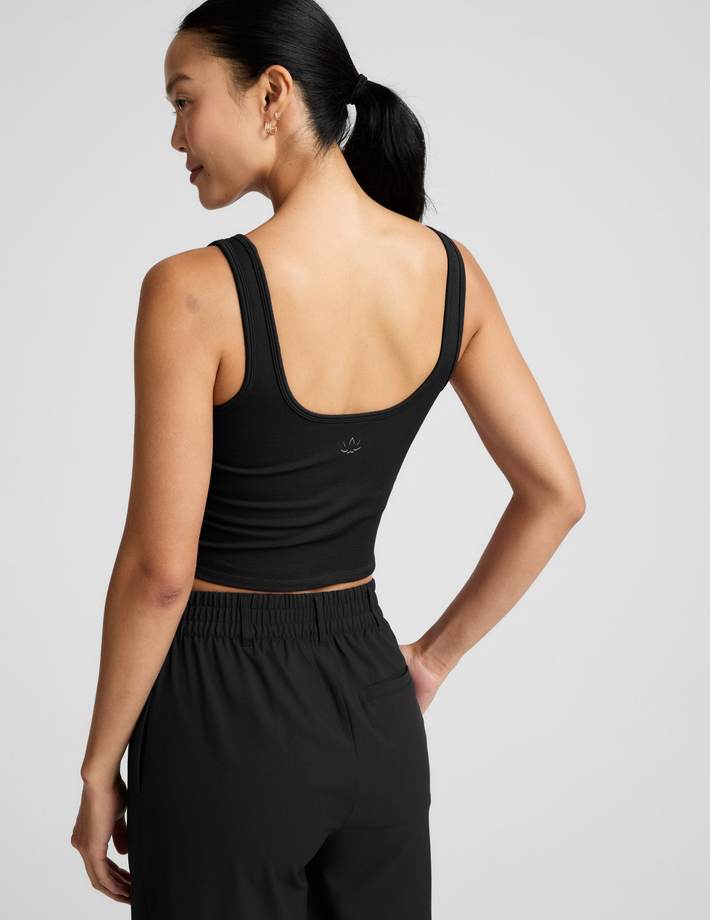 Woman is wearing a black ribbed tank and pants against a light gray background.
