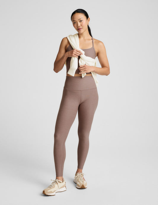 Woman wearing a brown cropped tank and leggings against a plain background.
