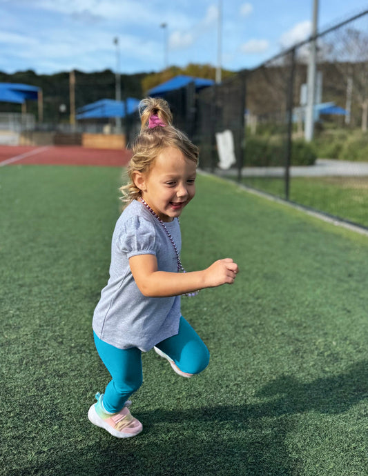 Toddler girl running in Blue Spacedye Toddler Legging™ paired with a grey puff-sleeve shirt and colorful sneakers.
