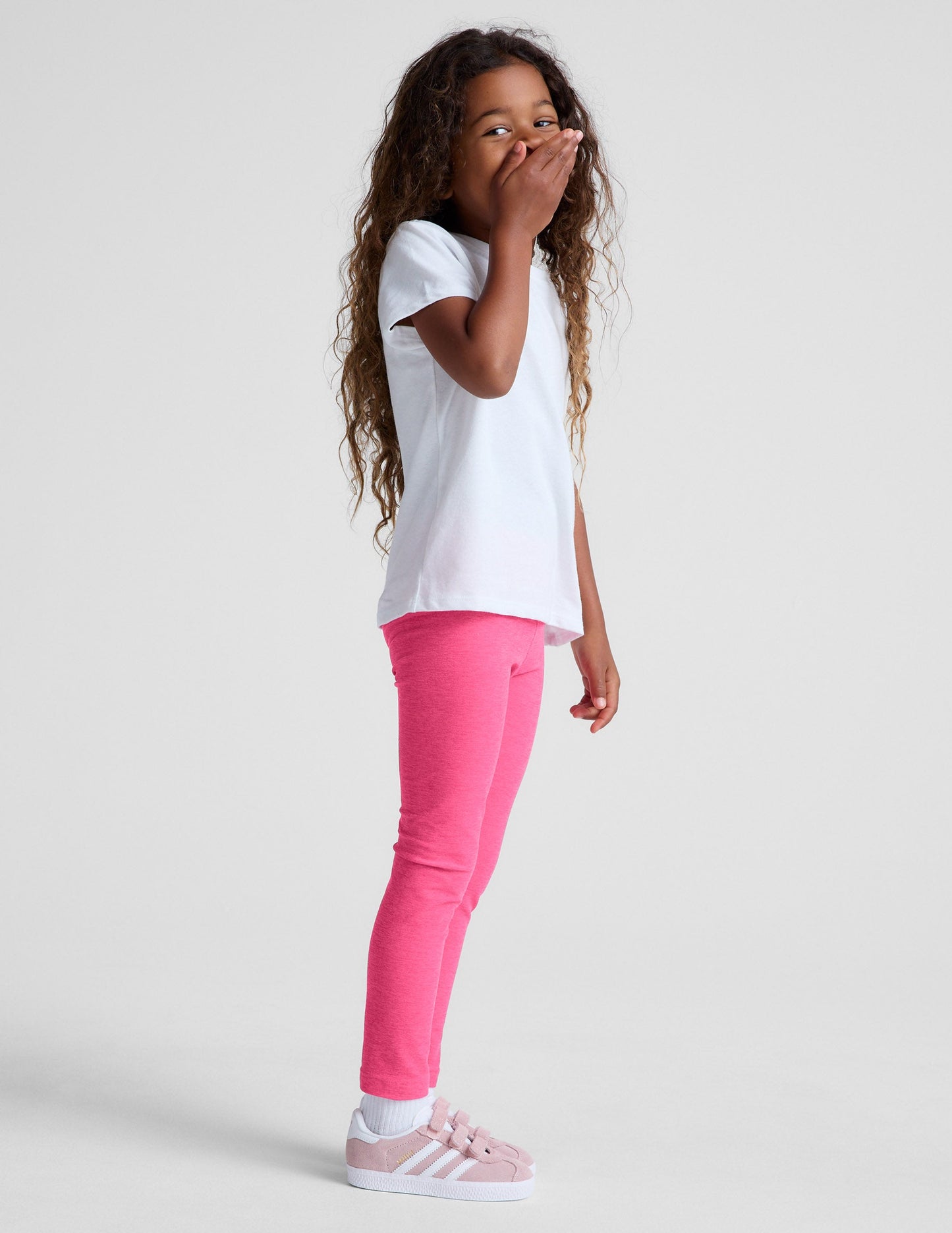 Girl in side profile wearing Pink Spacedye™ Toddler Legging paired with a white t-shirt and pink sneakers.